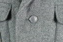 Close-up of grey wool Swiss army jacket showing plastic button with Swiss cross emblem and flap pockets.