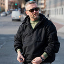 Man wearing black MIL-TEC German Military fleece-lined hooded windproof jacket outdoors in urban setting