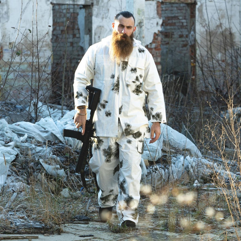 Man wearing A.Blochl German army style snow camo reversible pants and jacket holding a rifle in a ruined outdoor setting