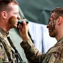 Two soldiers applying camouflage paint to each other's faces.