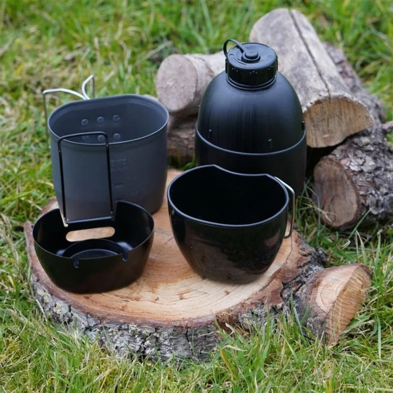 Black BCB multi-fuel cooking set with canteen, cup, and pouch on wooden stump in outdoor setting