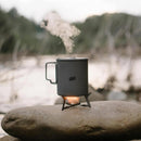 ESBIT solid fuel stove heating a pot outdoors on a rock, portable titanium camping gear with visible steam rising.