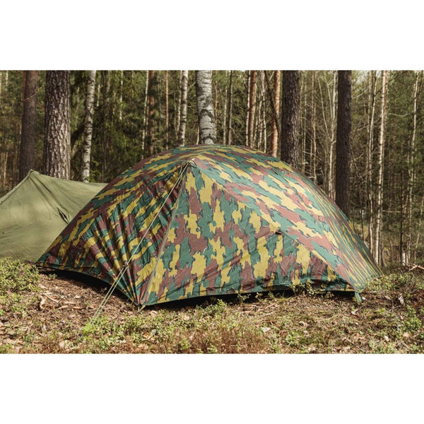 Belgian military two-person waterproof ripstop tent set up in a forest with camouflage pattern and stakes secured.