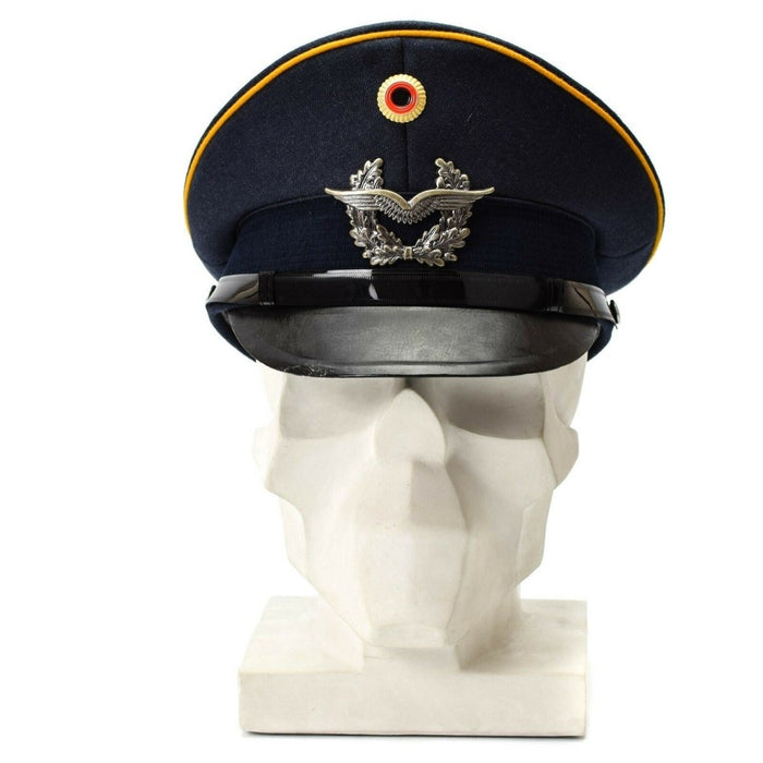 Vintage blauwe Duitse Luftwaffe luchtmacht vizierpet met militaire insignes en gele biezen weergegeven op witte buste