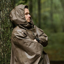 Person wearing vintage German army waterproof rain poncho with hood leaning against tree in forest setting