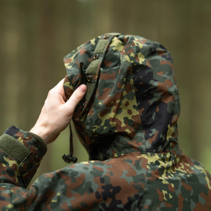 Close-up of a person adjusting the hood of a Mil-Tec German army Flecktarn waterproof parka jacket in a forest setting
