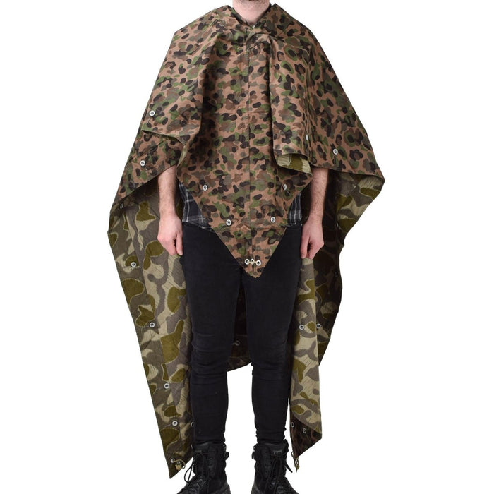 Persoon die een vintage waterbestendige pea dot splinter camoponcho-tent van het Oostenrijkse leger draagt met hoekbanden