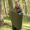 Man outdoors unrolling compact lightweight original British military gray sleeping pad in forest setting