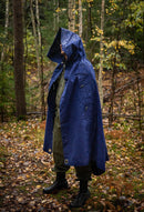 Person wearing blue waterproof Romanian military surplus tent tarpaulin as rain poncho in forest setting